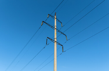 The top part of a tall power pole with wires and insulators against a clear blue sky