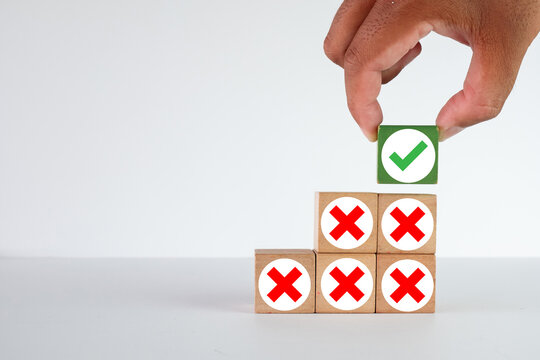 Hand placing a green checkmark block on top of a pyramid of red X marks.,Idea for business,finance,education,positive outcome,problem-solving,trial and error.,White background with coypspace.