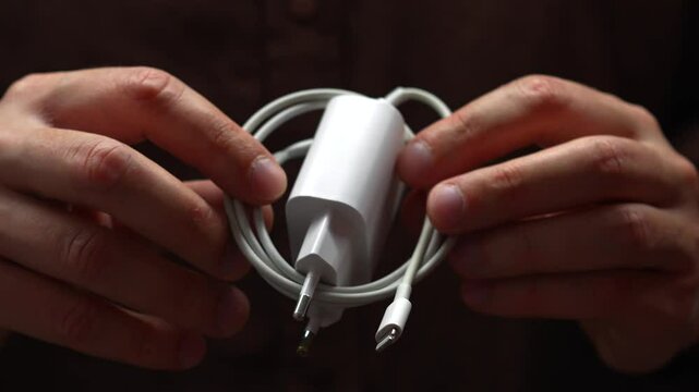 A man in brown clothes holds in his hands a coiled cable for charging a mobile phone.
Block and charger for electrical device.
Charging, battery, phone, cable, cable