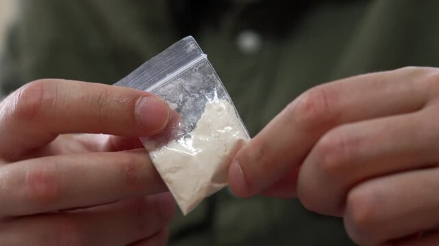 A man in a green shirt is holding a bag of drugs similar to heroin or cocaine.
White powder addict.
Drugs, harm, health, heroin