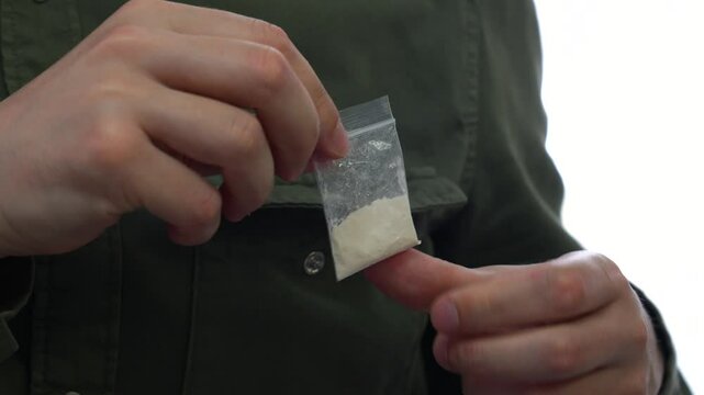 A man in a green shirt is holding a bag of drugs similar to heroin or cocaine.
White powder addict.
Drugs, harm, health, heroin