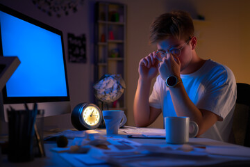 Young man working late at night at a desk with computer, feeling stressed and tired in a home office – concept of deadline pressure and burnout.