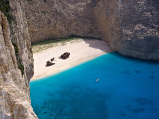 Direct aerial view of Navagio Beach with its famous shipwreck and vivid blue sea, surrounded by...