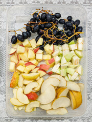 Top view of seeded black grapes, sliced red apples, guava, and pear in a transparent plastic container. Colorful fresh fruit mix, healthy snack, natural ingredients, clean eating