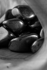 Pile of black rocks are in a bowl. The rocks are shiny and metallic. The bowl is on a wooden surface