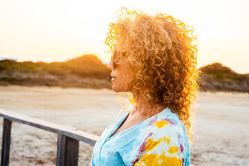 Joyful curly-haired woman wearing sunglasses enjoying the golden sunset in nature. Peaceful outdoor...