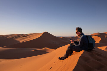 traveler using internet on mobile phone in remote place in desert, man with smartphone sitting in sand dunes, connection