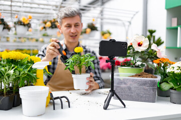A man is recording a gardening video with plants and flowers in a greenhouse.