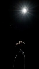 Silhouette of a person looking upwards towards a bright light source