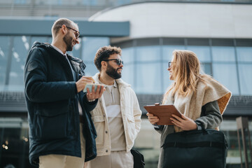 Three professional individuals are engaged in a cordial discussion, sharing ideas outdoors near a...