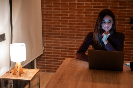 Young woman working late at night on laptop at home alone. Freelancer, student, focused on deadline, chatting online, battling insomnia, balancing work and study, nighttime productivity and digital li