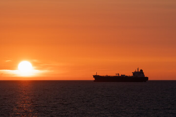Obraz premium A stunning seascape of the Baltic Sea at sunset. The silhouette of a ship on the horizon against a bright orange sky and the setting sun.