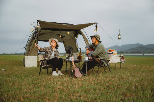 Young couple blogger enjoying outdoor lifestyle at tent site, Vlogging live scenic picnic moment with drinks and guitar music, Casual camping day with partner in nature, Relaxing in open field