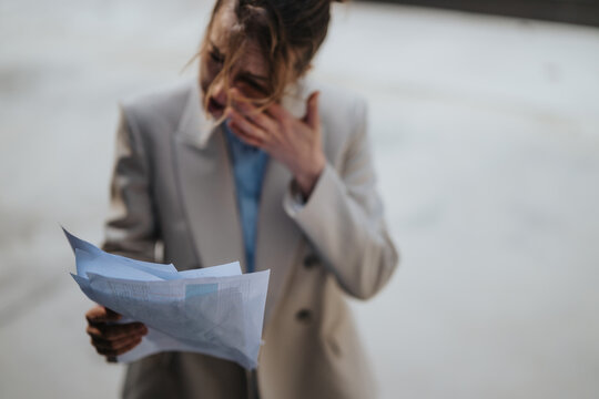 A frustrated woman in a blazer holding financial papers with a stressed expression, standing outside. The image captures the concept of business challenges and emotional strain.