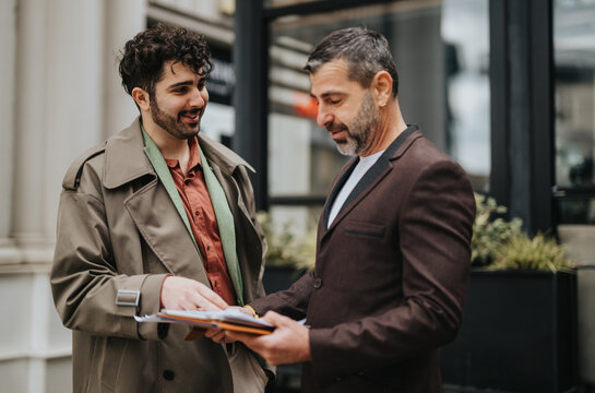 Two men engaging in a conversation while reviewing paperwork together outdoors, suggesting collaboration and discussion. - Powered by Adobe