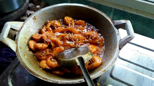 Close-up of spicy sweet and sour shrimp being cooked in a wok. Traditional Indonesian prawn dish made with chili, garlic, shallots, tomato sauce, and sweet soy sauce