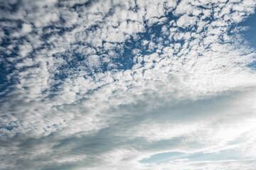 Scattered altocumulus clouds forming a textured pattern across a bright blue sky creating a soft...