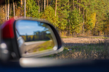 view in the rear view side mirror of a auto, driving a red car along the road