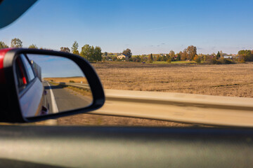 view in the rear view side mirror of a auto, driving a red car along the road