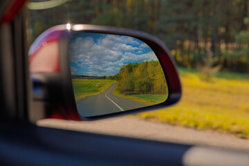 view in the rear view side mirror of a auto, driving a red car along the road