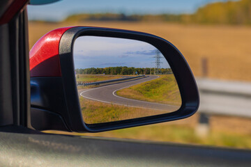 view in the rear view side mirror of a auto, driving a red car along the road