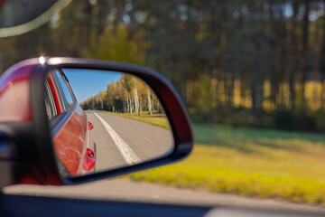 The sun is reflected in the mirror, evening road. View in the rear view side mirror of a auto,...