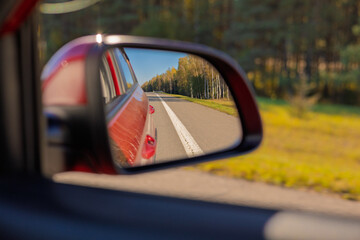 view in the rear view side mirror of a auto, driving a red car along the road