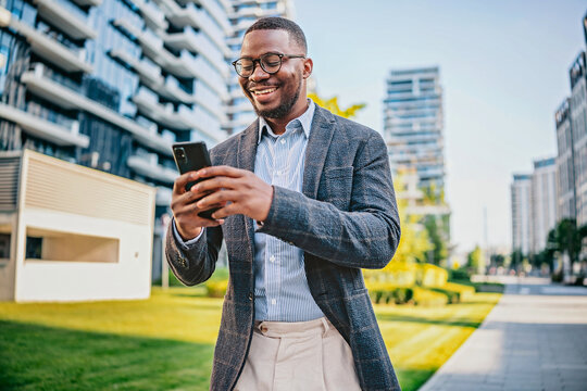 Young black businessman checks smartphone while walking in modern urban landscape during sunny day