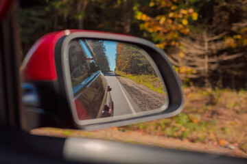 The sun is reflected in the mirror, evening road. View in the rear view side mirror of a auto,...