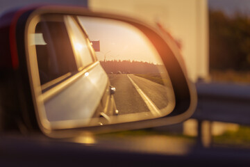 The sun is reflected in the mirror, evening road. View in the rear view side mirror of a auto,...