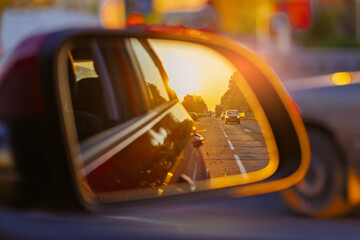 The sun is reflected in the mirror, evening road. View in the rear view side mirror of a auto,...