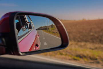 view in the rear view side mirror of a auto, driving a red car along the road
