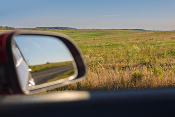The sun is reflected in the mirror, evening road. View in the rear view side mirror of a auto,...