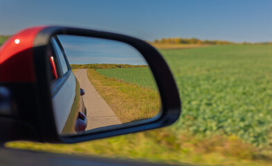view in the rear view side mirror of a auto, driving a red car along the road