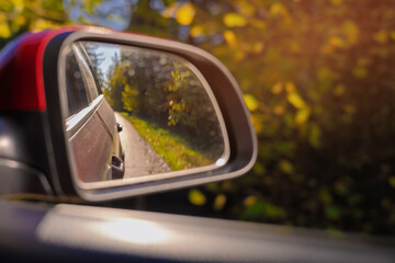 view in the rear view side mirror of a auto, driving a red car along the road