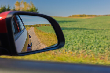 The sun is reflected in the mirror, evening road. View in the rear view side mirror of a auto,...