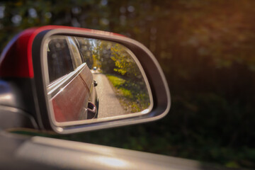 The sun is reflected in the mirror, evening road. View in the rear view side mirror of a auto,...