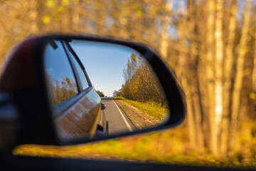 The sun is reflected in the mirror, evening road. View in the rear view side mirror of a auto,...