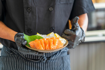 Japanese chef gives a thumbs-up to salmon. Chef cutting fish and making sashimi.