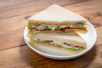 Sandwich with fresh vegetables and creamy salad dressing on a white plate on wooden background.