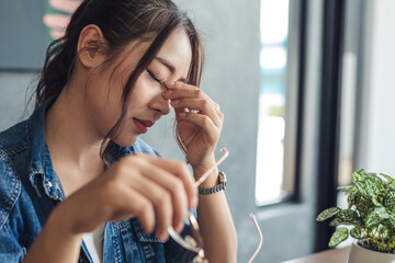 Stressed young female freelancer in her workplace, tired Asian businesswoman with headache while...