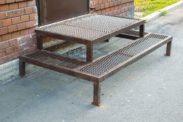 Small porch with two steps in front of brown door. Porch made of metal