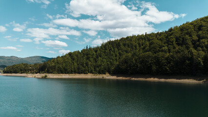 Quiet corner of Zaovine Lake surrounded by dense green forest and hills under a sunny spring sky....