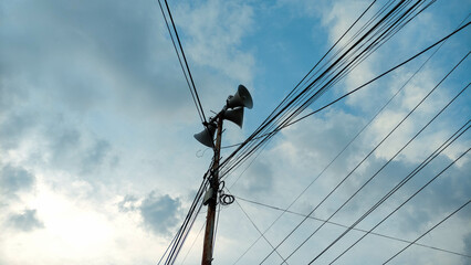 Rustic Utility Pole with Loudspeakers and Power Lines Against Cloudy Sky