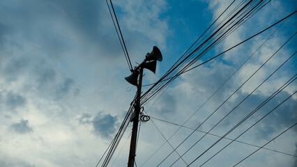 Rustic Utility Pole with Loudspeakers and Power Lines Against Cloudy Sky