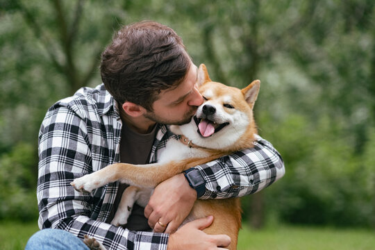 Young man in plaid shirt walking with shiba inu dog in summer park sunny day joyful outdoor activity pet companionship concept lifestyle