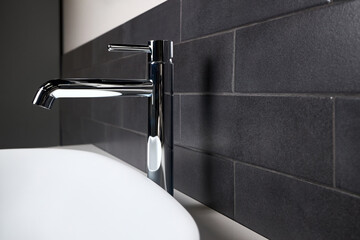 Interior detail of bathroom with washbasin sink with oval mounted overhead sink and faucet. Bathroom interior sink with black tiled wall modern flat minimalistic design side view close up copy space.