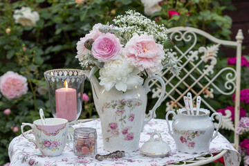 Tisch-Arrangement mit Blumenstrauß mit Rose, Pfingstrosen und Gypsophila, vintage Porzellan und Laterne im Sommergarten