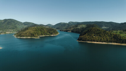 Naklejka premium A wide aerial view of Zaovine Lake winding through forested hills with village houses in Tara National Park, Serbia