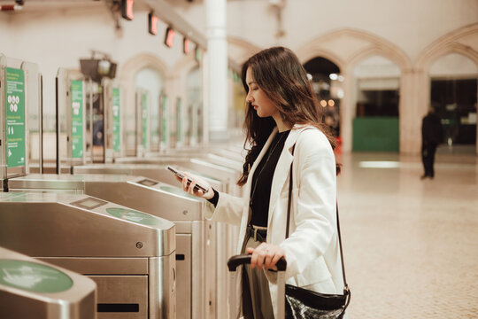 Young woman paying with smartphone via contactless NFC terminal and getting ready for travel at train station in Lisbon. Concept of business travel and individual tourism